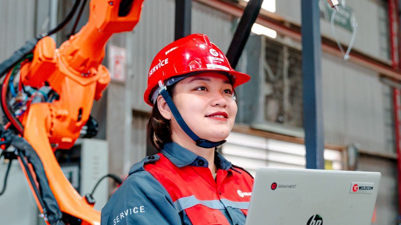 Ingeniera supervisando con un portátil un brazo robótico en una línea de producción automatizada